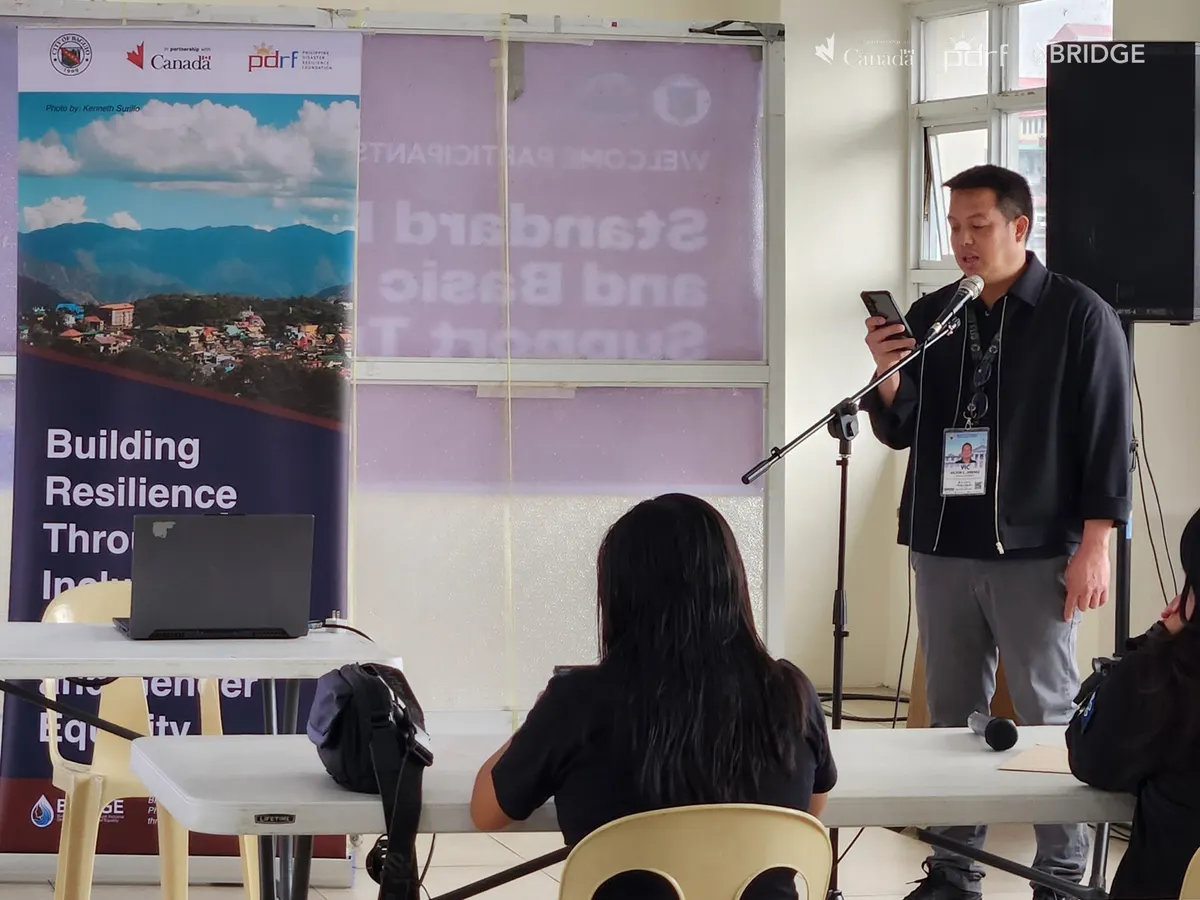 A speaker addressing participants at the Business Continuity Management training, beside a BRIDGE Project banner.