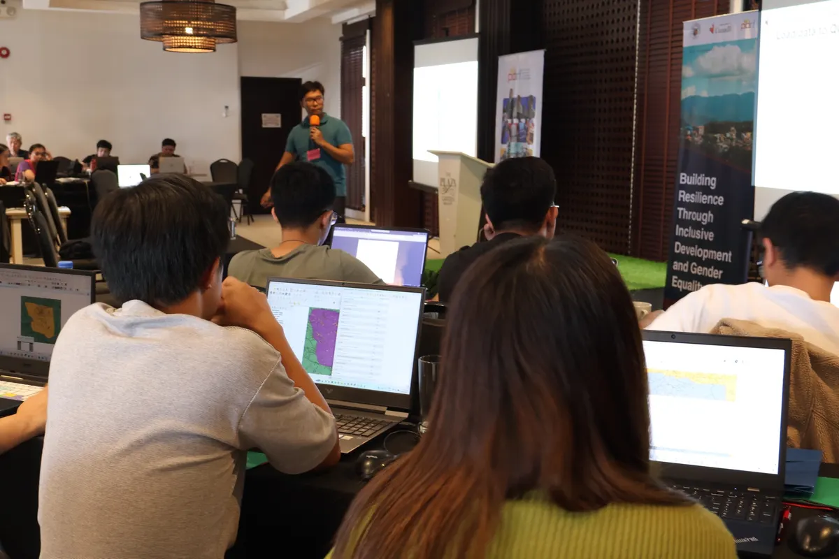 Participants working on GIS maps on their laptops while a facilitator presents at the front of the room.
