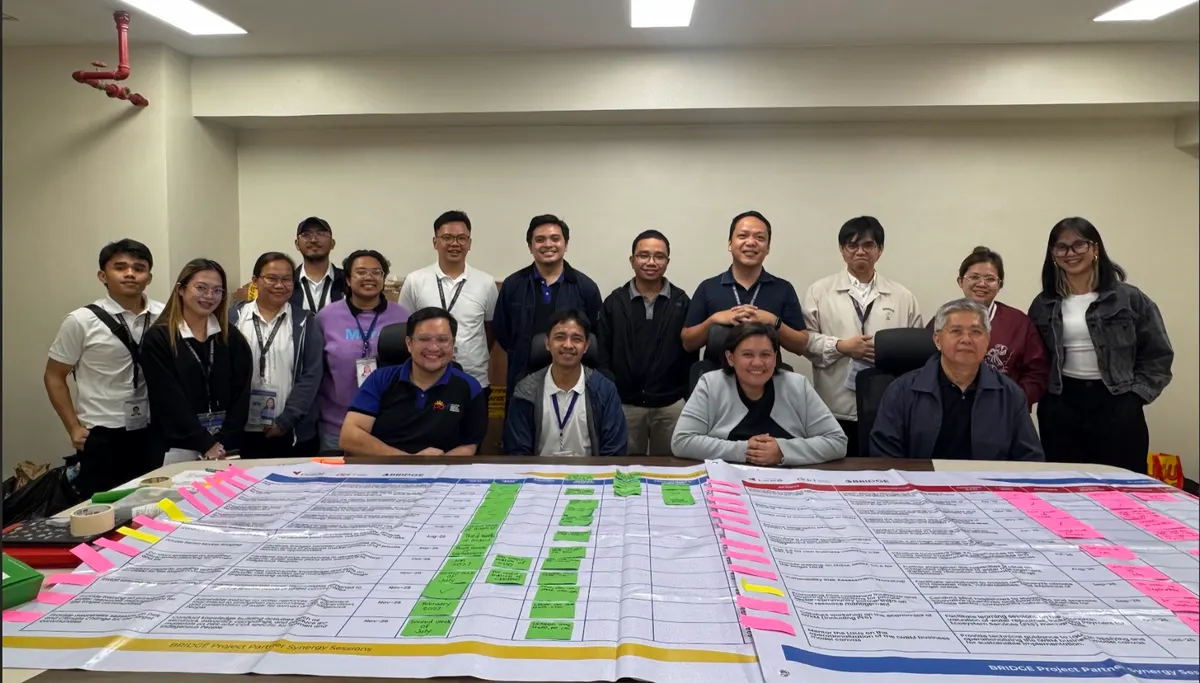 Workshop participants behind a large printed implementation calendar covered in coloured sticky notes at a BRIDGE Project Partner Synergy Session.